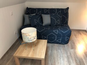 A modern living room with a dark blue sofa adorned with geometric patterns, a small wooden side table, and a lamp with a map design. - Cottage by Orne River with garden and fishing, Pets allowed (Mézières-sur-Ponthouin)