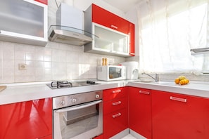 Une cuisine moderne avec des meubles de couleur rouge, une cuisinière en acier inoxydable, un four à micro-ondes et un four encastré.