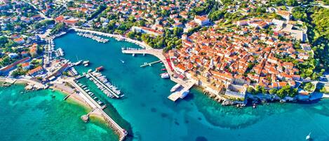 An aerial view of a coastal town with a marina, dense residential area, and a prominent castle-like structure.