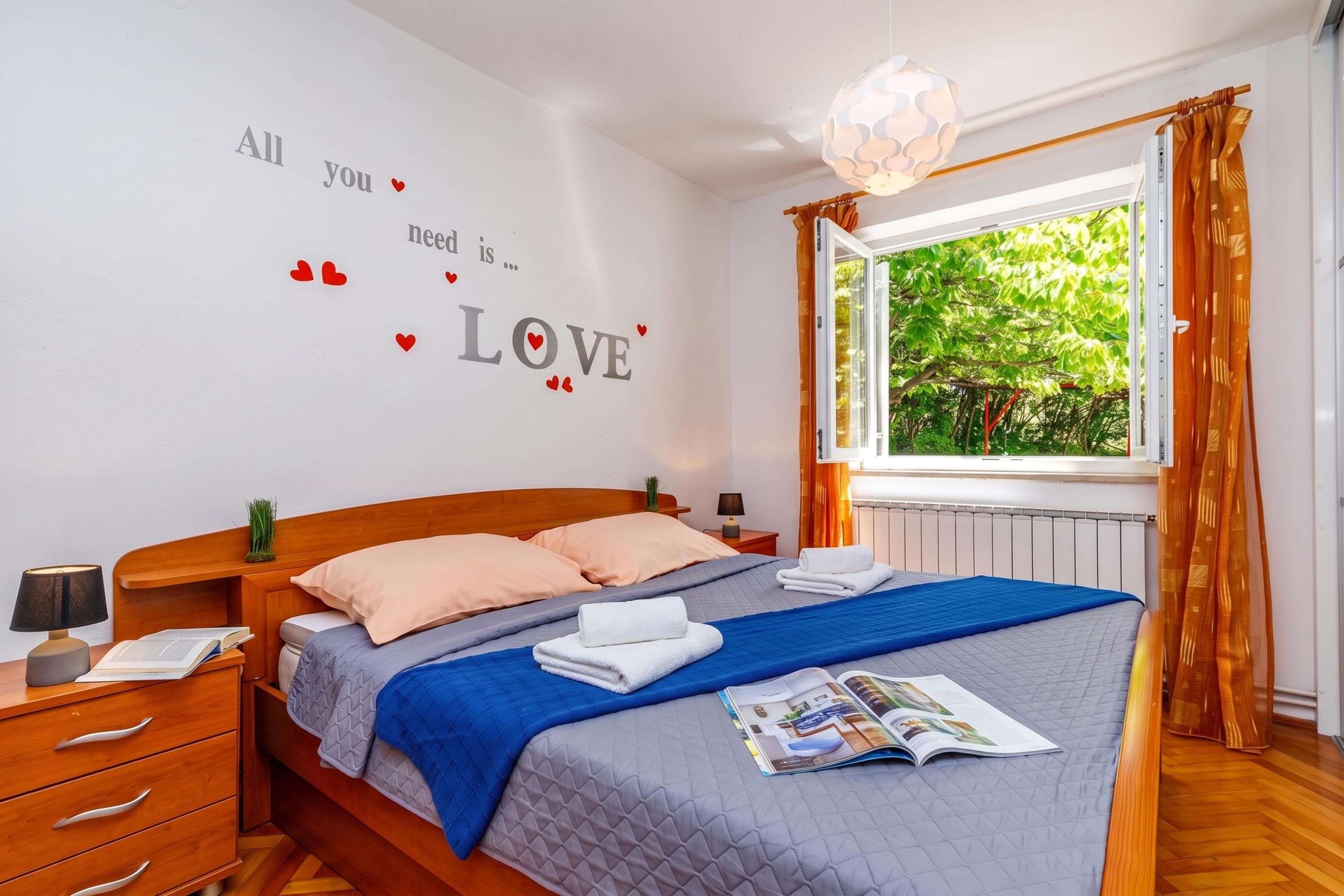 Ein Schlafzimmer mit einem Bett, einem Nachttisch, einer Lampe, einem Fenster mit Vorhängen und einer Wand mit einer Liebesdekoration.
