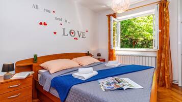 Quarto com cama, mesa de cabeceira, abajur, janela com cortinas e decoração romântica na parede.