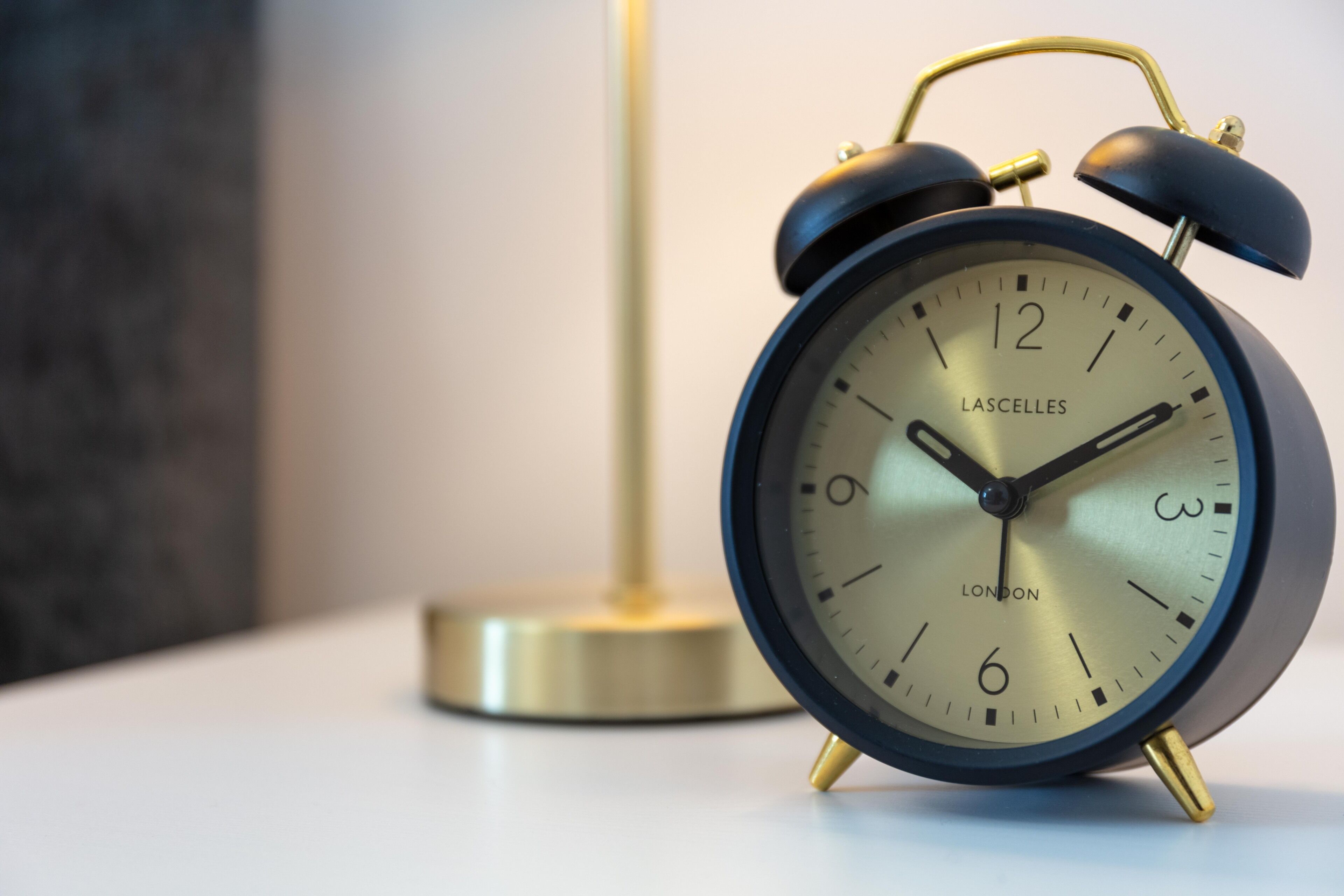 A black and gold Lascelles alarm clock with a gold base, placed on a white surface.