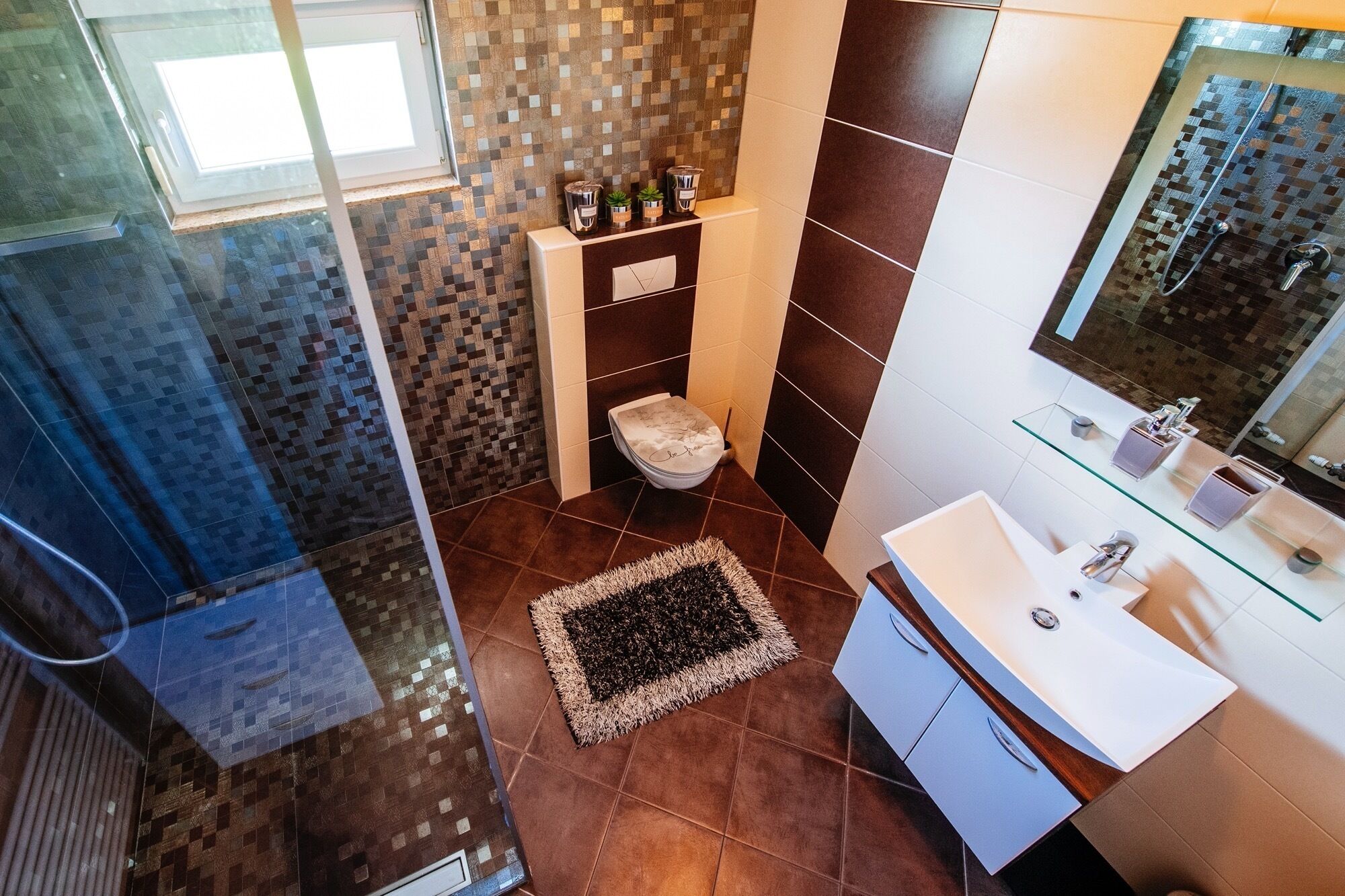 A modern bathroom with a glass shower enclosure, a toilet with a decorative lid, a sink with a glass countertop, and a mirror above the sink.