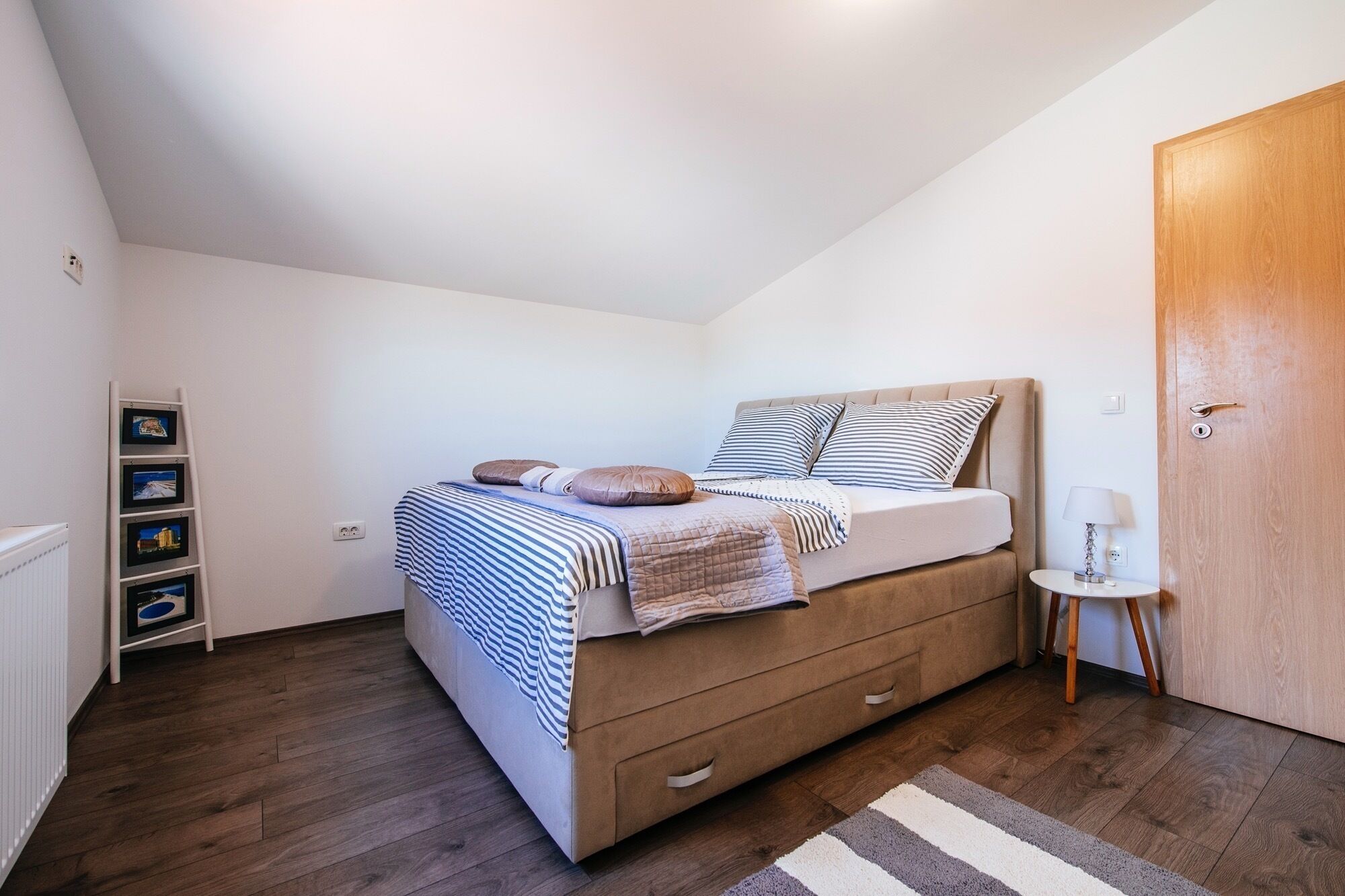 Une chambre à coucher avec un lit, une table de chevet, une lampe, une porte en bois et un radiateur.