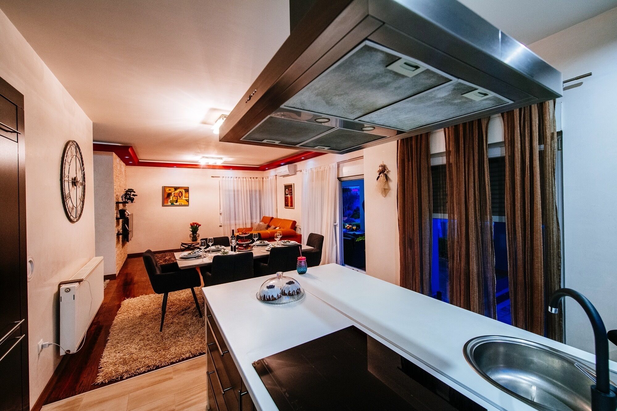 A modern kitchen with a central island, a dining area with a sofa, and a view of the city through large windows.