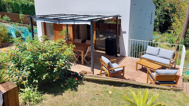 A modern house with a patio area featuring a wooden table and chairs, a sofa, and a covered seating area.