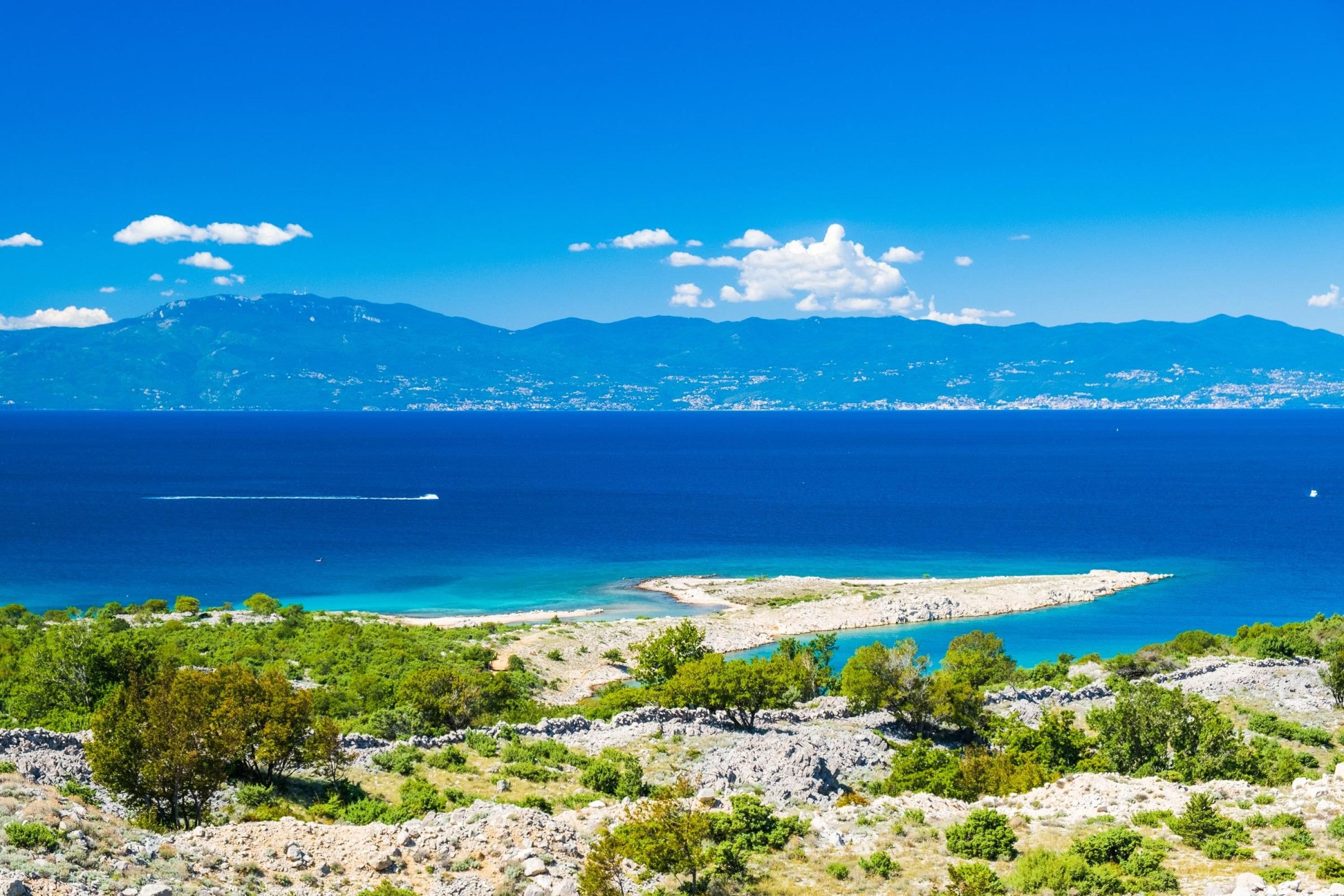 Un paysage côtier offrant une vue dégagée sur la mer, avec un terrain rocheux et des montagnes à l’horizon.