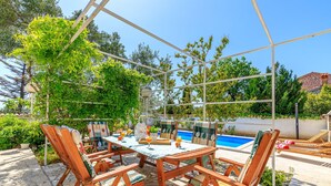 A covered outdoor area with a pool, wooden chairs, and a table with drinks. - Exclusive Pool Escape Near Sea (Krk)