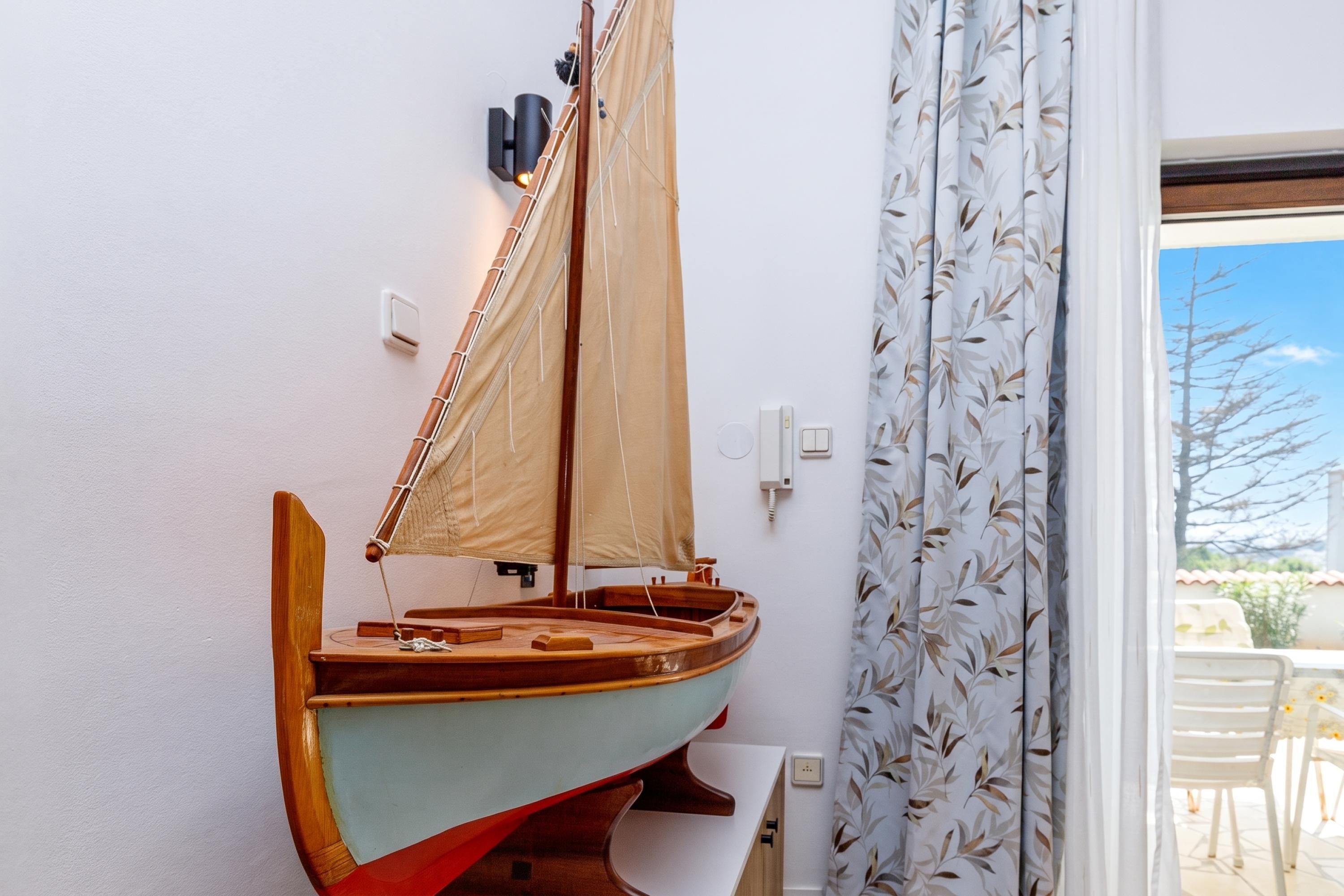 Un velero de juguete sujeto a la pared, una ventana con vistas al exterior y una puerta con cortina.