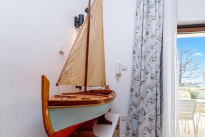 Un modèle de voilier fixé au mur, une fenêtre donnant sur l’extérieur et une porte avec un rideau.