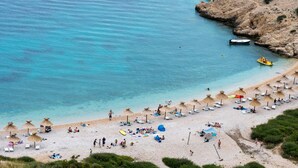 A beach with umbrellas and lounge chairs, a rocky coastline, and a boat in the water. - Exclusive Pool Escape Near Sea (Krk)