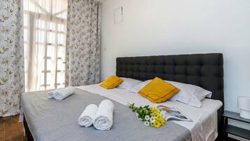 Una cama bien hecha con toallas enrolladas, dos almohadas, una revista y un pequeño ramo de flores.