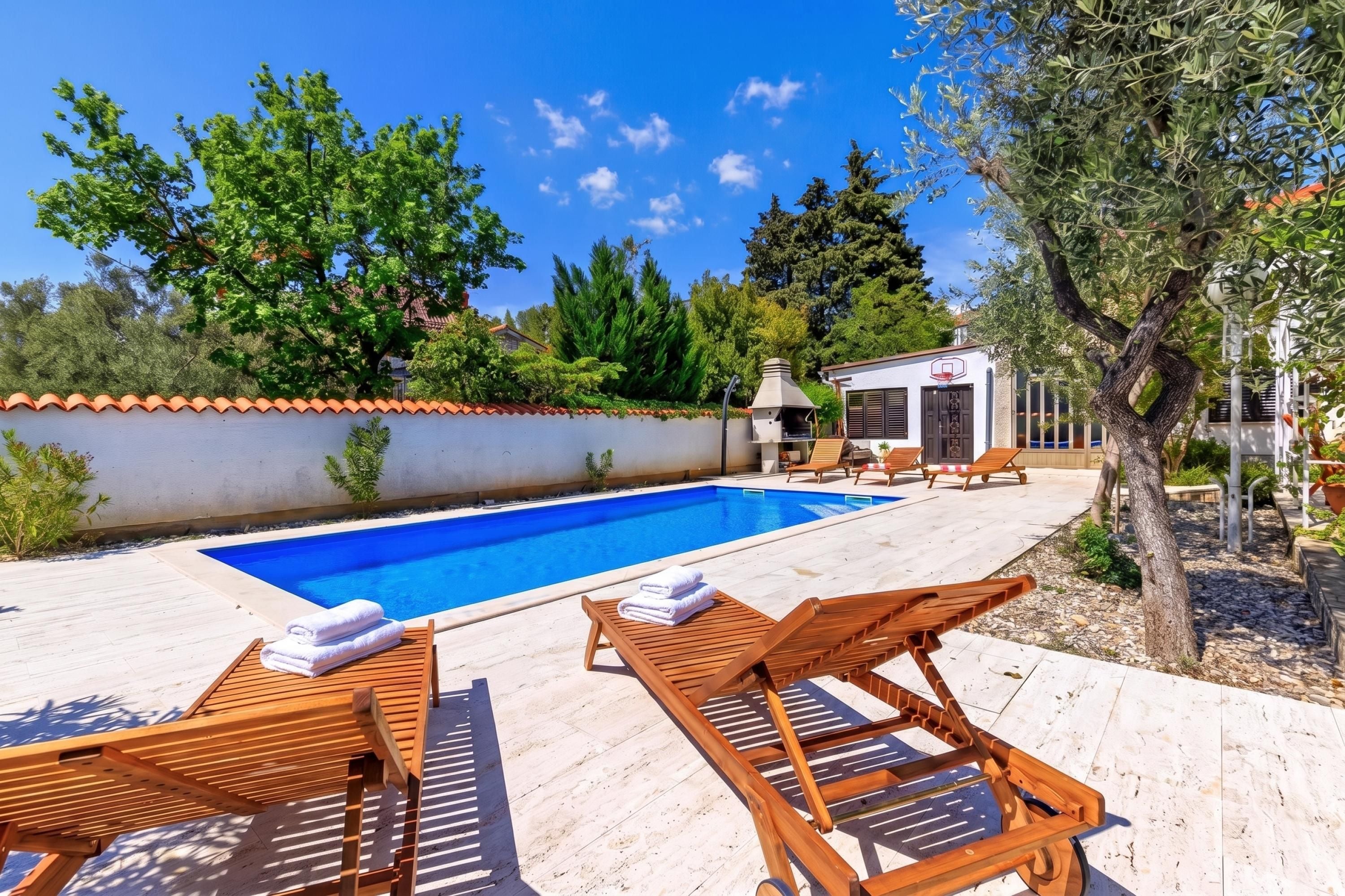 A swimming pool with lounge chairs and a small building with a basketball hoop.