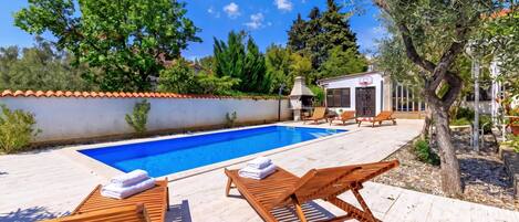 A swimming pool with lounge chairs and a small building with a basketball hoop.