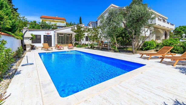 A swimming pool with lounge chairs, a building with a balcony, and a clear blue sky. - Exclusive Pool Escape Near Sea (Krk)