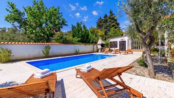 Une piscine avec des chaises longues et un petit bâtiment équipé d’un panier de basket.