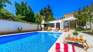 A swimming pool with a red and white towel, a wooden table with drinks, and a barbecue grill. - Exclusive Pool Escape Near Sea (Krk)