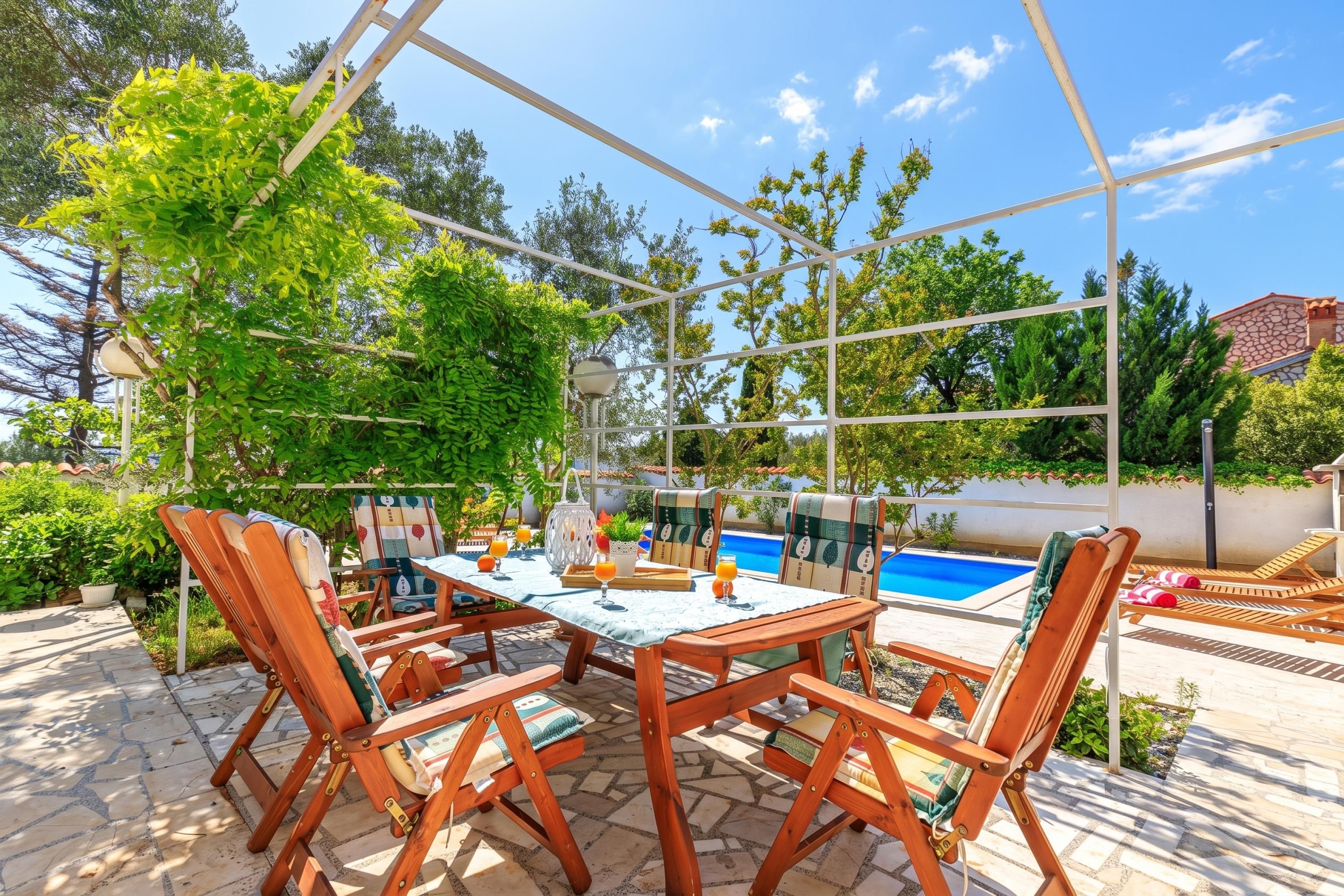 An outdoor patio with a pool, wooden furniture, and a clear sky.
