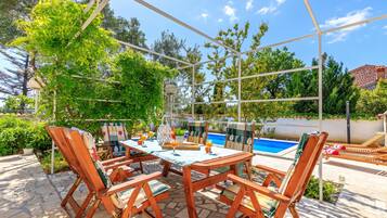 Un patio exterior con piscina, mobiliario de madera y cielo despejado.