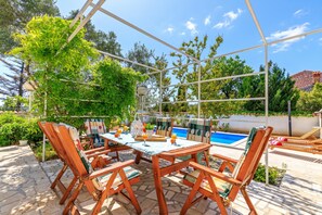 Un patio exterior con piscina, mobiliario de madera y cielo despejado.