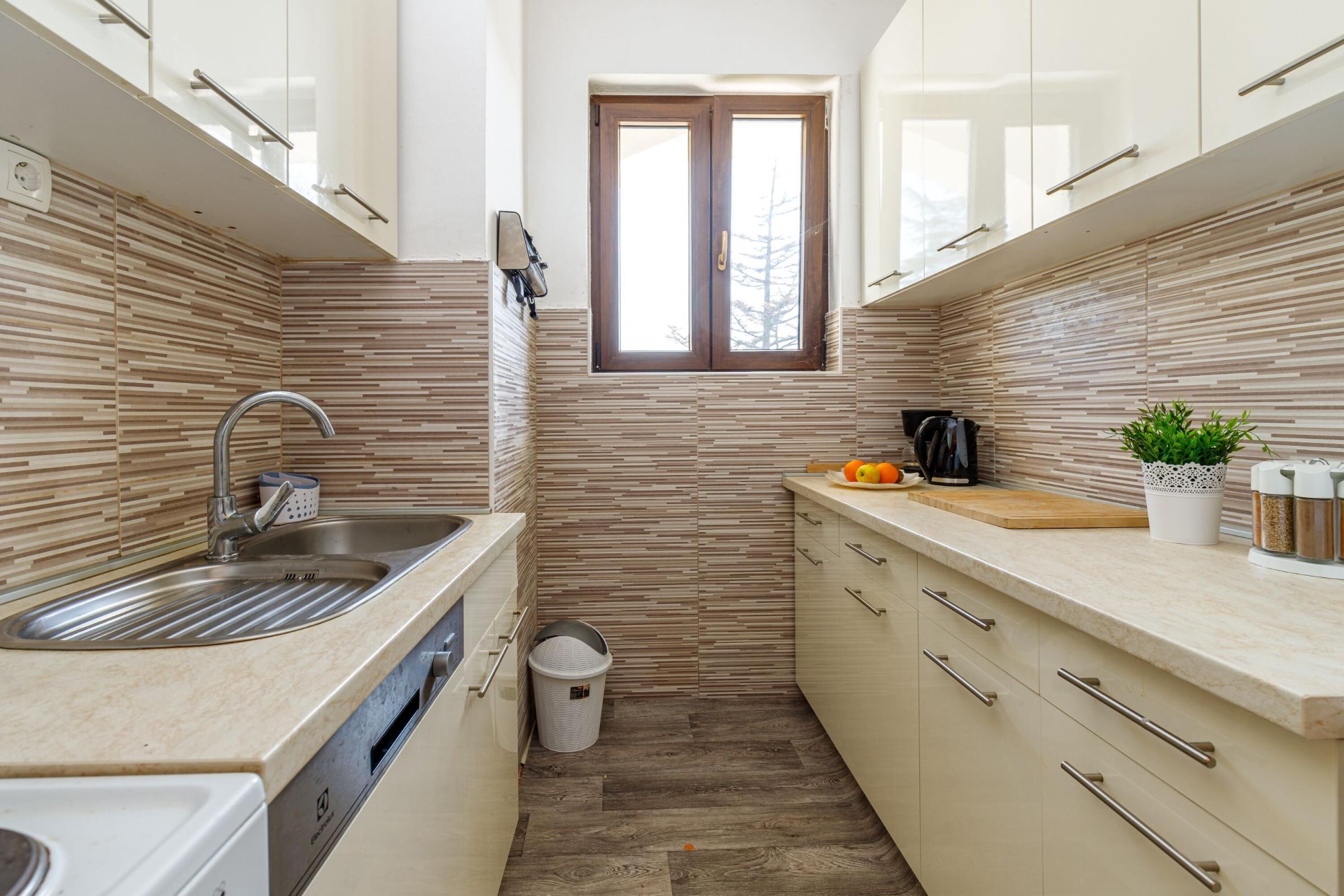 A compact kitchen with a built-in dishwasher, a window, and a small trash bin.