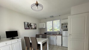 A compact kitchen with white cabinets, a dining table with chairs, a TV, and a window with a view of greenery.