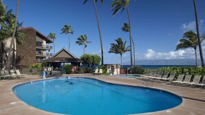 A swimming pool with lounge chairs, a building with a stone facade, and palm trees. - Papakea Resort - Beautiful 1 BR Ocean View Suite - NO Resort Fee (Lahaina)