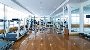 Un'ampia palestra con diverse attrezzature cardio e per l'allenamento della forza, ampie finestre e un pavimento in legno lucido.
