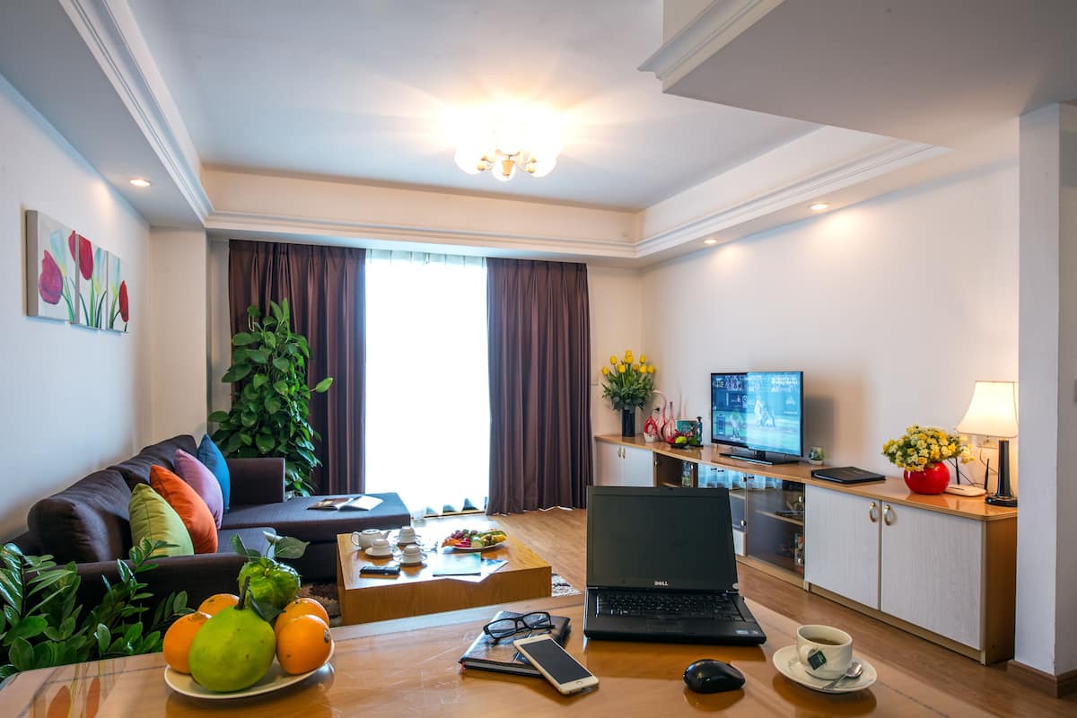 Ein modernes Wohnzimmer mit einem braunen Sofa, einem Couchtisch mit Früchten, einem Laptop und einem Fernseher.