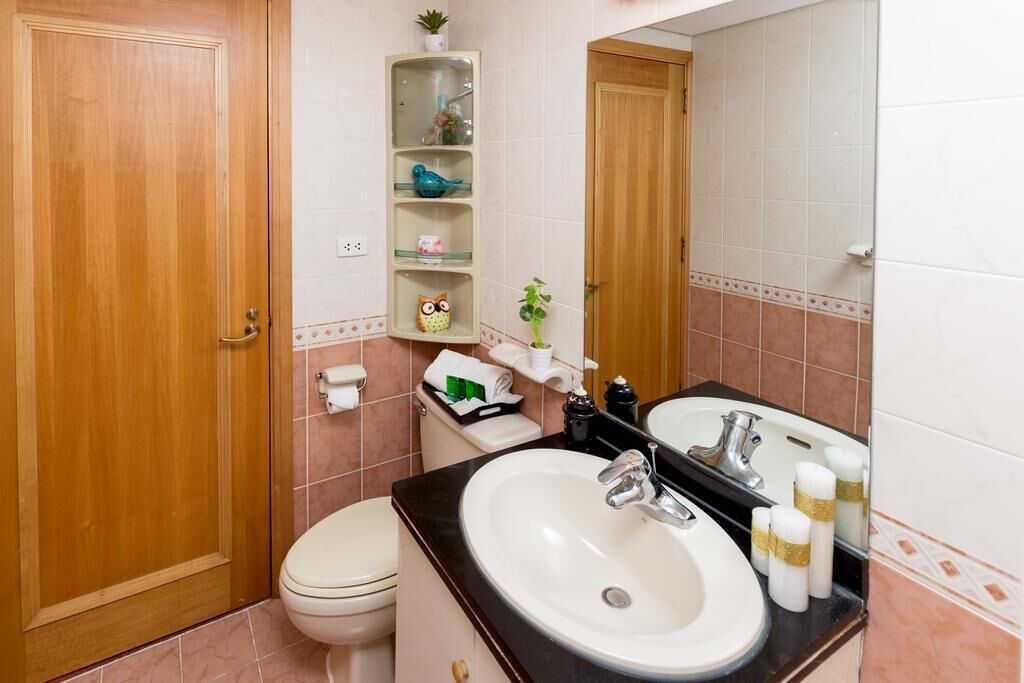 Een badkamer met toilet, wastafel en spiegel. Er zijn planken met toiletartikelen en een kleine plant.