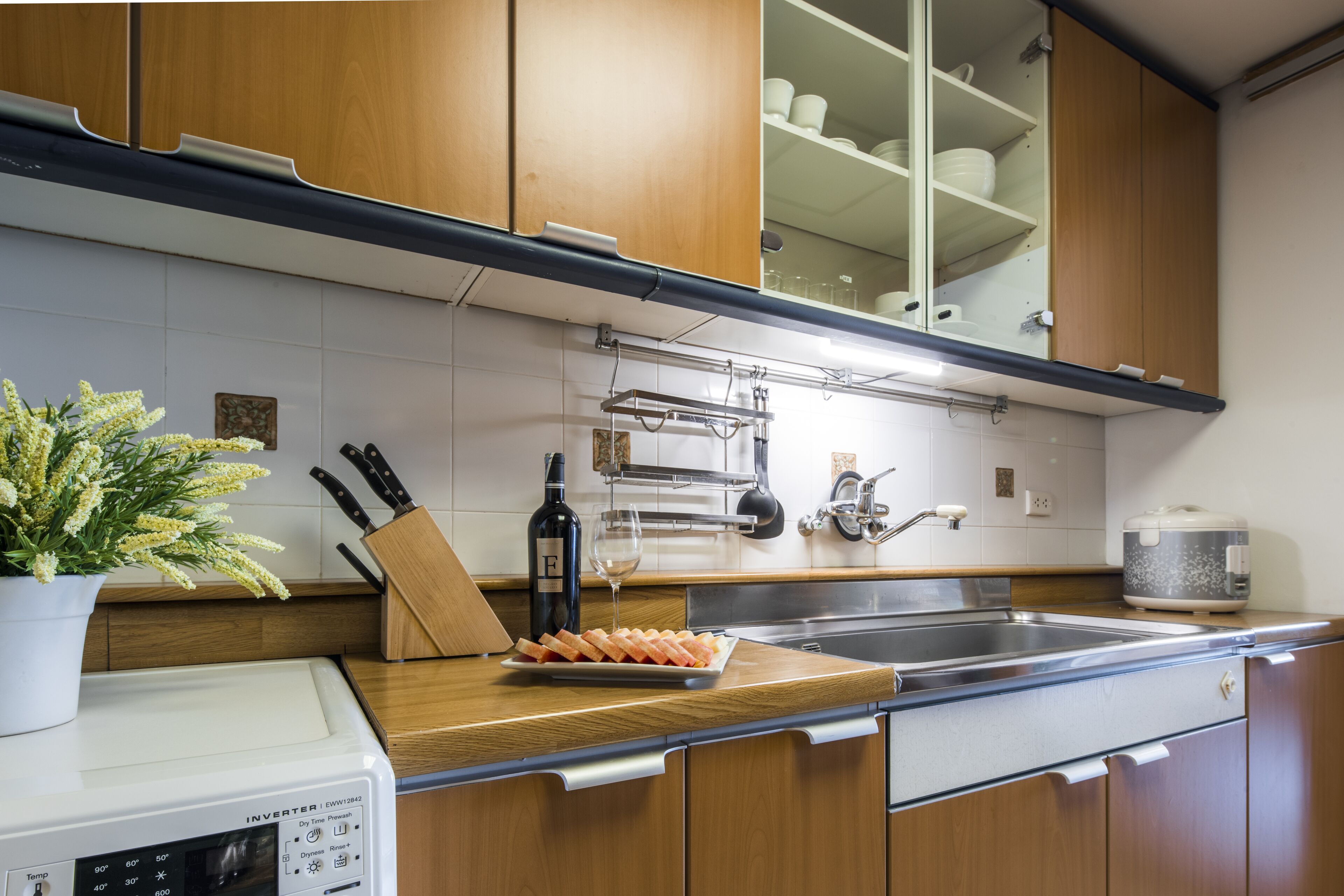 A modern kitchen with wooden cabinets, a built-in oven, a sink, and a countertop with a potted plant and a knife block.