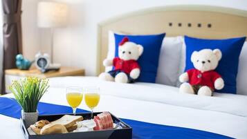 Habitación de hotel con una cama, dos osos de peluche, una bandeja con comida y bebidas, y una mesita de noche con una lámpara y un reloj.