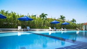 Una piscina con piastrelle blu, poltrone da relax bianche e ombrelloni blu.