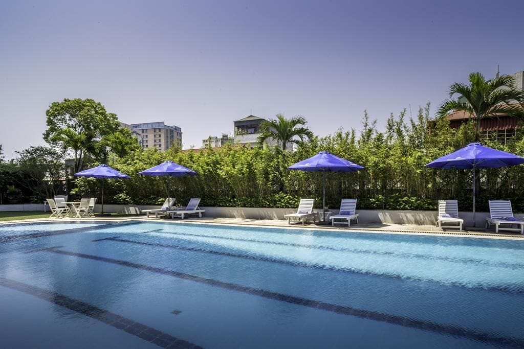 Une piscine à l’eau bleue, entourée de chaises longues blanches et de parasols bleus.