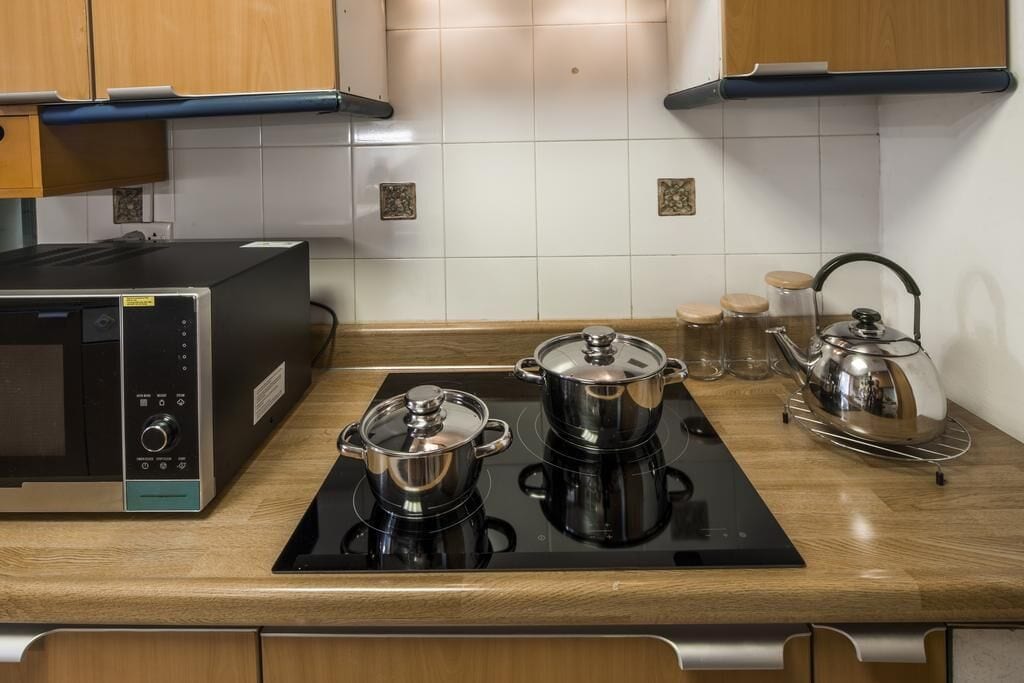 A kitchen with a built-in stove, two pots, a kettle, and a microwave.