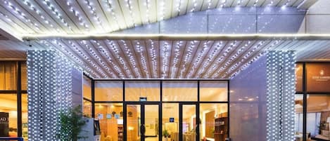 Entrada de hotel con diseño moderno, fachada de vidrio y un dosel de luces.