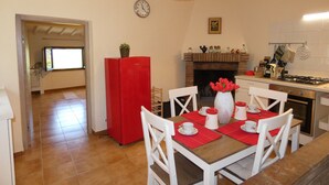 Una cocina con un refrigerador rojo, sillas blancas, una mesa de comedor con individuales rojos y un reloj en la pared.