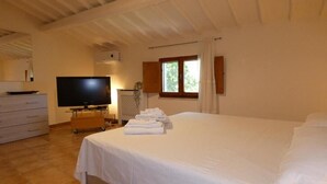 Un dormitorio con una cama, televisión, cómoda y ventana con cortinas.