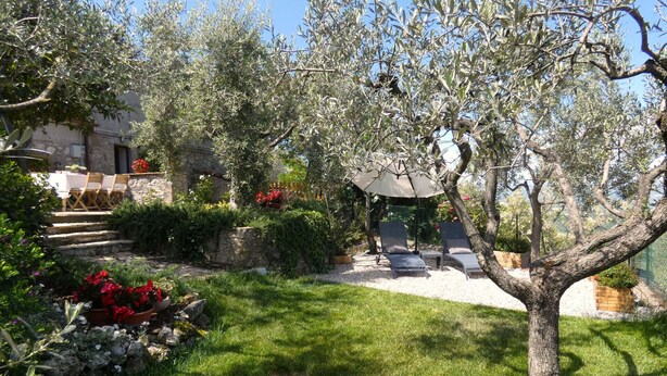 Un jardín con muro de piedra, mobiliario exterior y una pérgola.