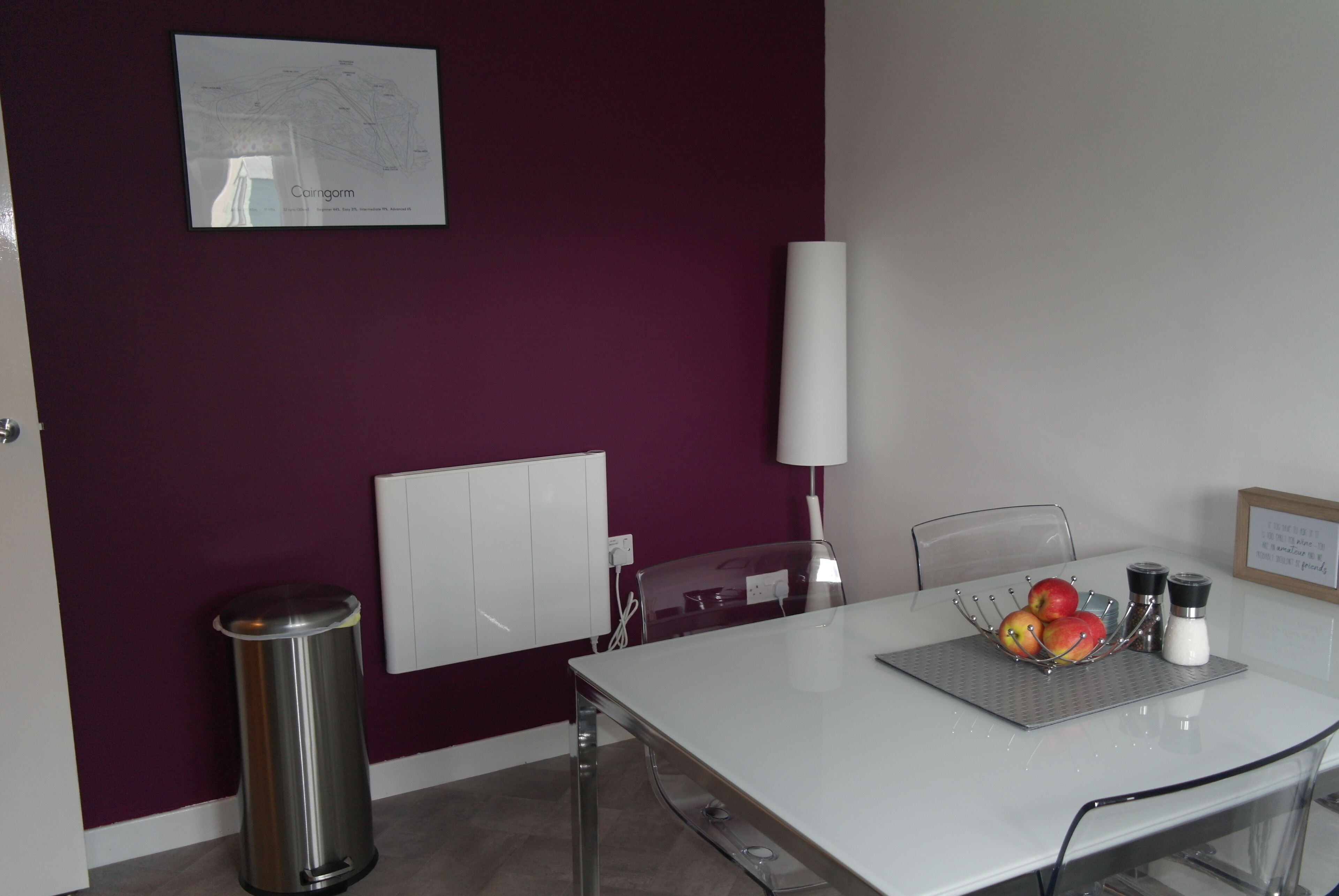 Una habitación moderna con una mesa blanca, paredes moradas, un mapa en la pared y un cubo de basura.