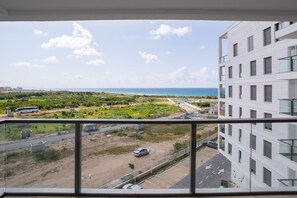 A view from a balcony overlooking a coastal area with a parking lot, a road, and a building with multiple windows. - Sunny Haven Sea View Escape by Sea N Rent (Nahariya)