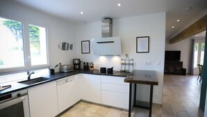 Een moderne keuken met witte kastjes, een inbouwoven, een broodrooster en een spoelbak. Een raam zorgt voor natuurlijk licht en uitzicht op groen.