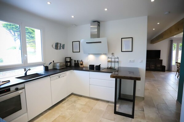 A modern kitchen with white cabinets, a built-in oven, a toaster, and a sink. There is a window providing natural light and a view of greenery outside.