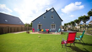 Een tweelaags huis met een terras, een omheinde achtertuin en een heldere lucht.