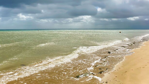 Een strand met helder water, een zandstrand en een bewolkte lucht.
