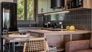 A modern kitchen with a built-in island, a refrigerator, a microwave, and a window providing natural light. - Moschato Estate Villas (Σβορωνάτα)