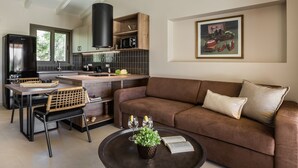 A modern kitchen with a dining area, a brown sofa, and a painting on the wall. - Moschato Estate Villas (Σβορωνάτα)