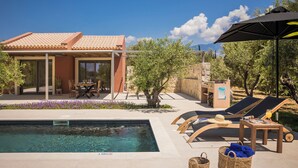 A poolside area with a clear pool, lounge chairs, a table, and a covered seating area. - Moschato Estate Villas (Σ βορωνάτα)