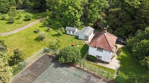 Luchtbeeld van een pand met een tennisbaan, een huis met een rode pannendak en omliggend groen.