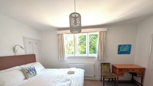 Un dormitorio con cama, escritorio, silla, radiador, ventana con cortinas e iluminación colgante.